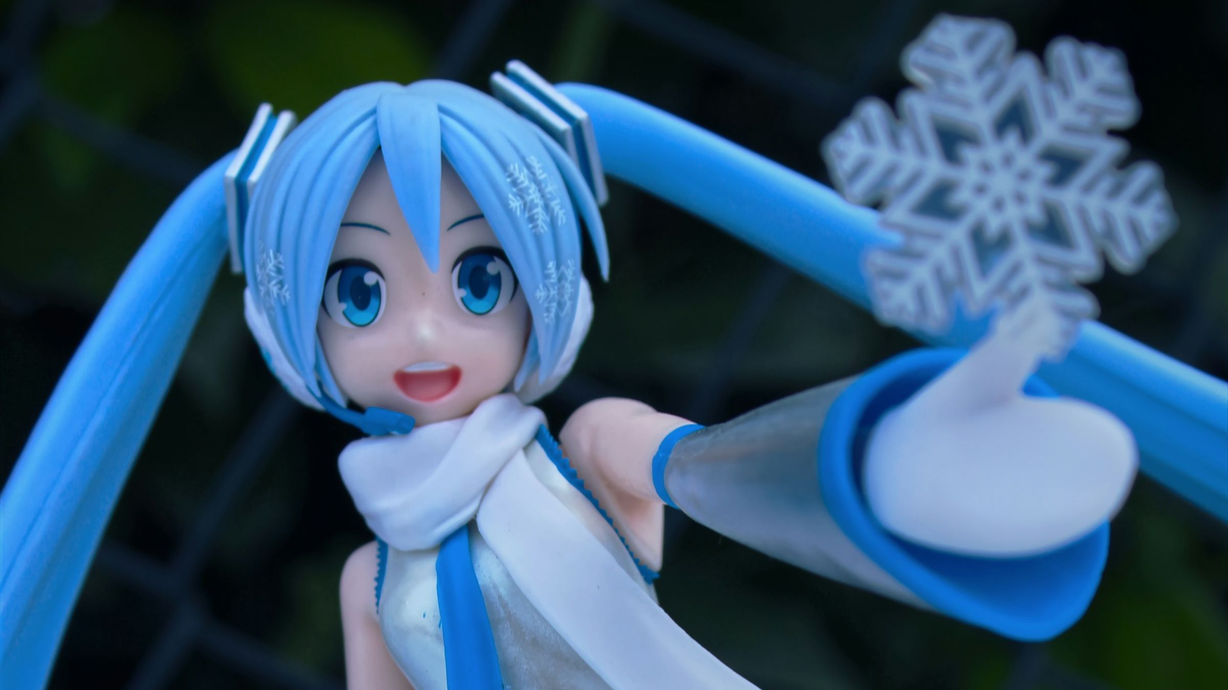 A Hatsune Miku figure, with long turquoise hair, standing in snow